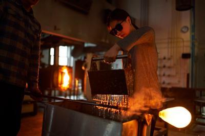 student blowing glass at the glory hole